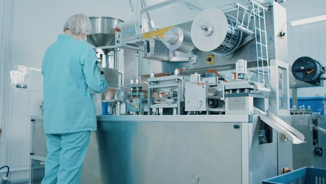4K Blister Packing Machine. Woman works at the workplace. Tablet pharmaceutical blister packaging machine in supplement drug manufacture. Pharmaceuticals production line