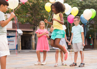 Joyful children playing with balloons and jumping rope outdoors. - obrazy, fototapety, plakaty