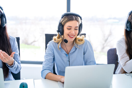 Friendly telephone operator woman with headset having conversation with client, showing excellent communication skills and attentive customer service, surrounded by female colleagues at call center.