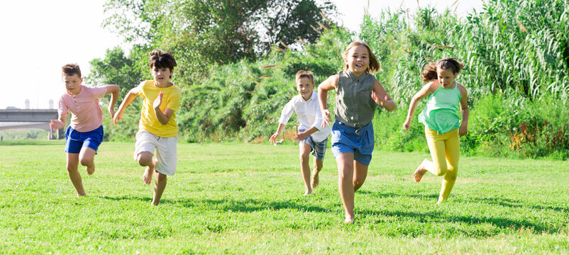Happy preteen friends having fun in summer city park, running together on green meadow..