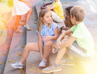 Happy tweenagers friends spending time together in city streets during summer vacations, sitting on...