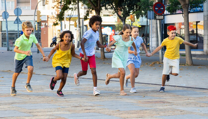 Fototapeta na wymiar Group of cheerful tweenagers of different nationalities running together along city street on summer day. Happy healthy kids concept..