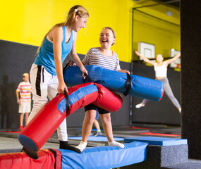 Expressive tween girl fighting by soft pugil stick with her female friend while standing on...