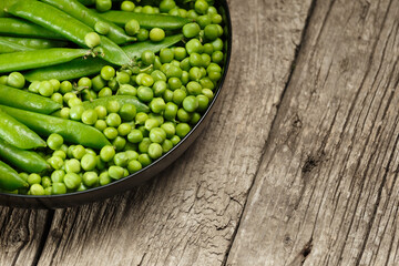 Fresh green peas in pods and peeled green peas in a round plate on a wooden background, copy space.