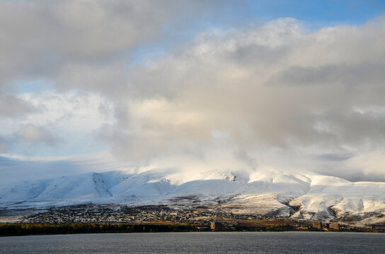 Сalm water surface of Lake Sevan and snow capped mountains under sky with low clouds. Famous natural landmark of Armenia