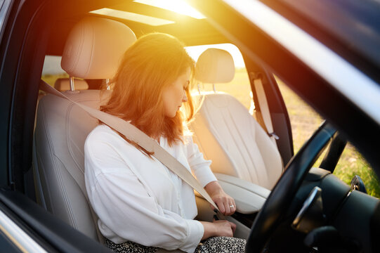 Pretty business lady fastens seat belt in new modern technological car. Happy woman fastening her seatbelt while sitting at the steering wheel of her car. Buckle up and drive safe.