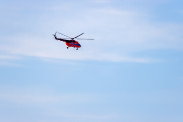 Fototapeta na wymiar A red helicopter flies against a blue sky. Passenger and cargo air transportation. Aviation transport services. Travel and tourist helicopter flights. Delivery of goods by air.
