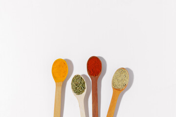 wooden spoons filled with spices and herbs - turmeric, paprika and oregano on a white isolated background. Space for your text or design