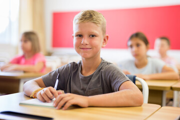 Fototapeta na wymiar Small american school boy sitting at the desk in classroom at lesson in primary school