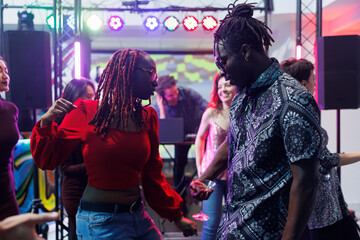 Young african american couple dancing and making moves to live music beats in crowded nightclub. Boyfriend and girlfriend dancers partying together on dancefloor in dark club