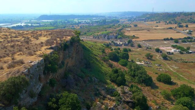 In this captivating aerial stock video, the remarkable ruins of the ancient city of Perge in conteprorary city of Antalya, Turkey are shown. The camera gracefully glides above, offering a panoramic