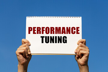 Performance tuning text on notebook paper held by 2 hands with isolated blue sky background. This message can be used as business concept about performance tuning.