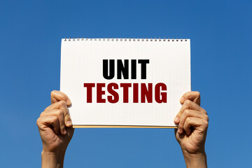 Unit testing text on notebook paper held by 2 hands with isolated blue sky background. This message can be used as business concept about unit testing.