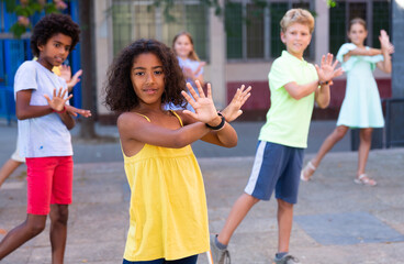 Smiling curly african american preteen girl dancing modern choreography with group of tweenagers on...