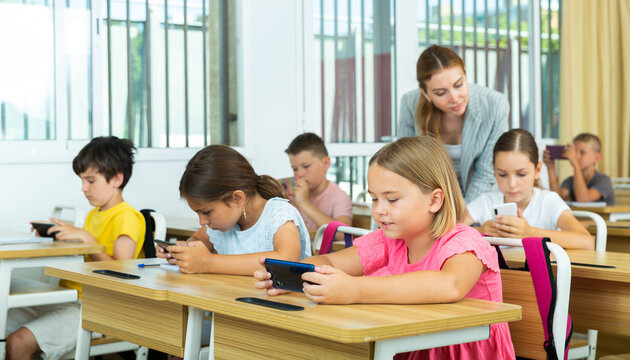 Absorbed interested preteen school children using mobile phones to watch game-based learning materials during lesson in classroom