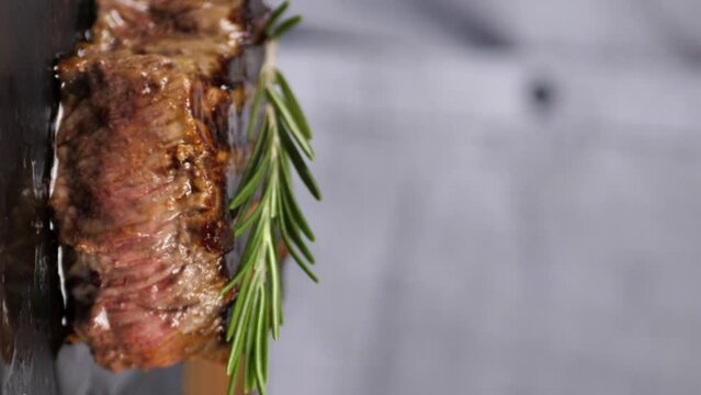 faceless chef garnishes beef steak with rosemary sprig. Vertical screen