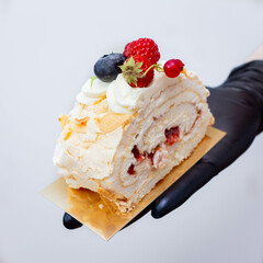 Meringue Roulade Slice on a Golden Stand Held by a Hand in a Black Glove