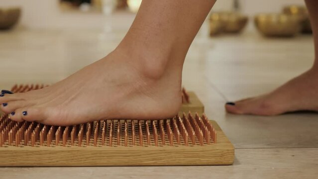 Female feet stand on boards with nails, close up. Barefoot female standing on yoga nails board. Sadhu board