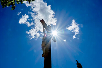 Cross with Jesus Christ from behind and below with clouds in the background, back-lit by a direct view of the sun