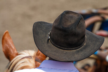 A man is wearing a black western style hat and a dark blue shirt. He is leaning on a rail at a...