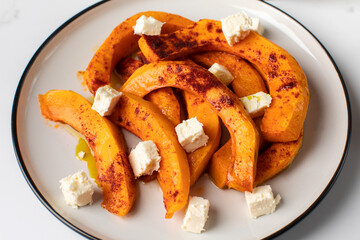 Baked pumpkin slices with spices and cubes of feta cheese. Pumpkin dishes.