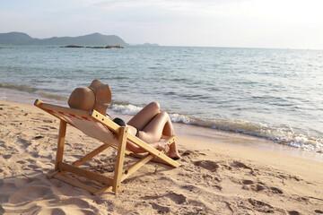 Sexy beautiful young woman posing in a black swimwear bikini reclining on the sea beach