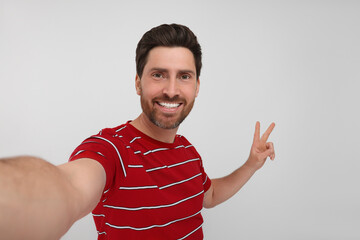 Smiling man taking selfie and showing peace sign on white background