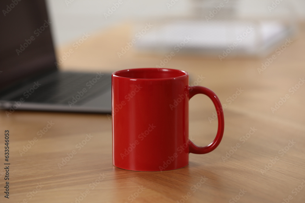 Poster Red ceramic mug and laptop on wooden table at workplace