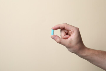 Man holding pill on beige background, closeup. Space for text