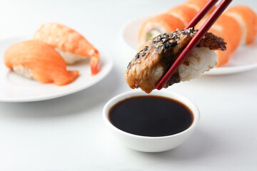 Dipping tasty nigiri sushi with smoked eel into soy sauce on white table, closeup