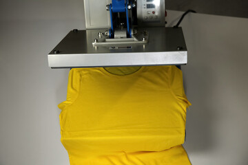 Printing logo. Heat press with yellow t-shirt on white table