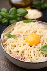 Bowl of tasty pasta Carbonara with basil leaves and egg yolk on wooden table, closeup