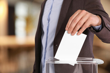 Obraz premium Man putting his vote into ballot box on blurred background, closeup