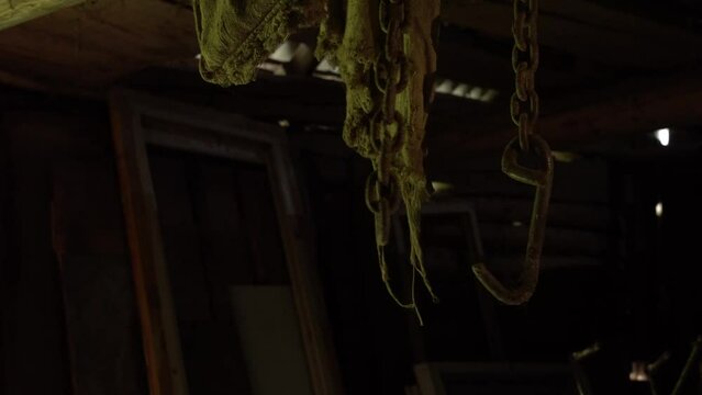 Rusty chains hang from the ceiling and dangle in an abandoned basement, a metal chain and rusty hook move in an old barn