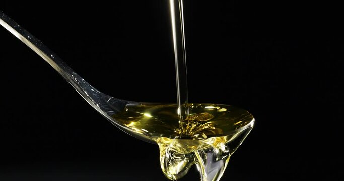 Olive oil pouring on spoon over black background, Slow motion

