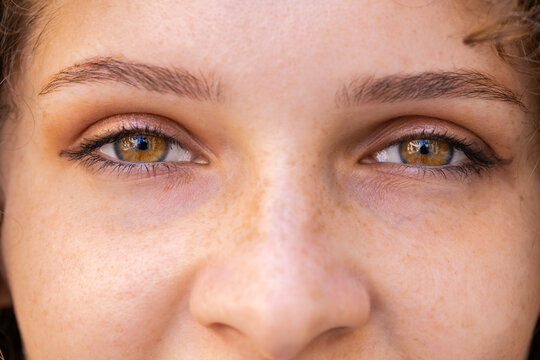 Extreme close-up macro portrait of face. Young adult beautiful pretty woman's eyes looking at camera. Brown eyes of teen girl female. Caucasian woman opening blinking eyes, smiling. Laser correction
