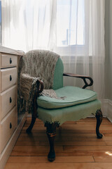vue sur un fauteuil confortable avec appuie bras en bois dans une pièce avec éclairage naturel d'une fenêtre avec voilage blanc et une commode