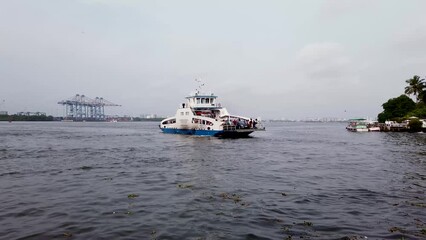 A Pan view of a Water craft with tourists and Automobiles is cruising in the Arabian sea near Kochi city in Kerala, India.