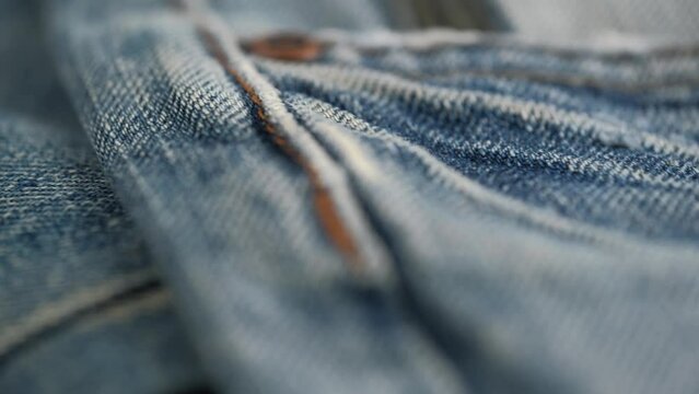 rotation of details of jeans trim closeup. metal rivets on pockets of denim trousers and decorative orange stitching on edges of fabric. abstract background, denim texture. low view angle.