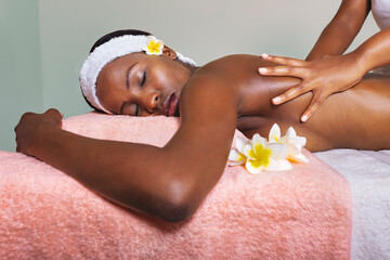 african woman at a spa centre laying on the bed , having a massage and skin moisturize, pampering...