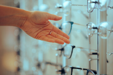 Hand Reaching for Eyeglasses Pair In a Optical Store. Customer choosing  new glasses from a rack display
