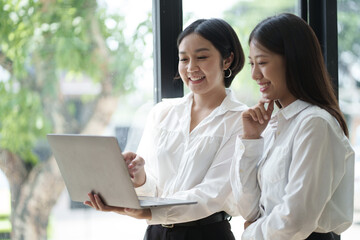 Two professional smart Asian business woman working together in the office room, discussion information from laptop.