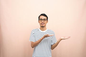 Asian man with glasses wearing casual striped shirt, whispering pose while pointing to the side....