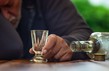 Ein Mann schläft betrunken an einem Tisch. Eine leere Flasche und ein Schnapsglas sind vor ihm. - obrazy, fototapety, plakaty