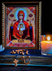 The time for prayer. Wooden Rosary on an ancient prayer book. Icon of the Mother of God and Jesus. Lighted candle