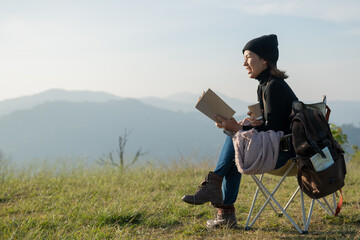woman traveler drinks coffee and read book with view of mountain landscape. young tourist woman drinks hot drink from cup and enjoyed the scenery in mountains. trekking concept.