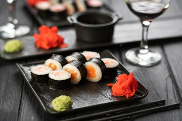 Philadelphia maki sushi rolls with salmon, cheese cream on slate board and glasses of red wine.