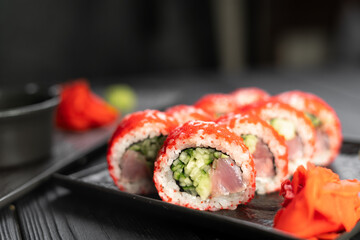 Delicious sushi roll california with tuna cucumber cheese and masago caviar on top on a stone plate on black background.