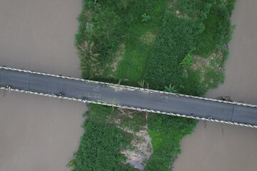 Aerial view of the long bridge over the brown watery river. the river delta is overgrown with green...
