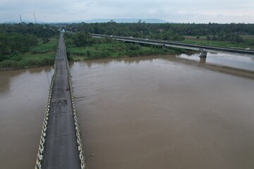 Aerial view of the long bridge over the brown watery river. the river delta is overgrown with green...